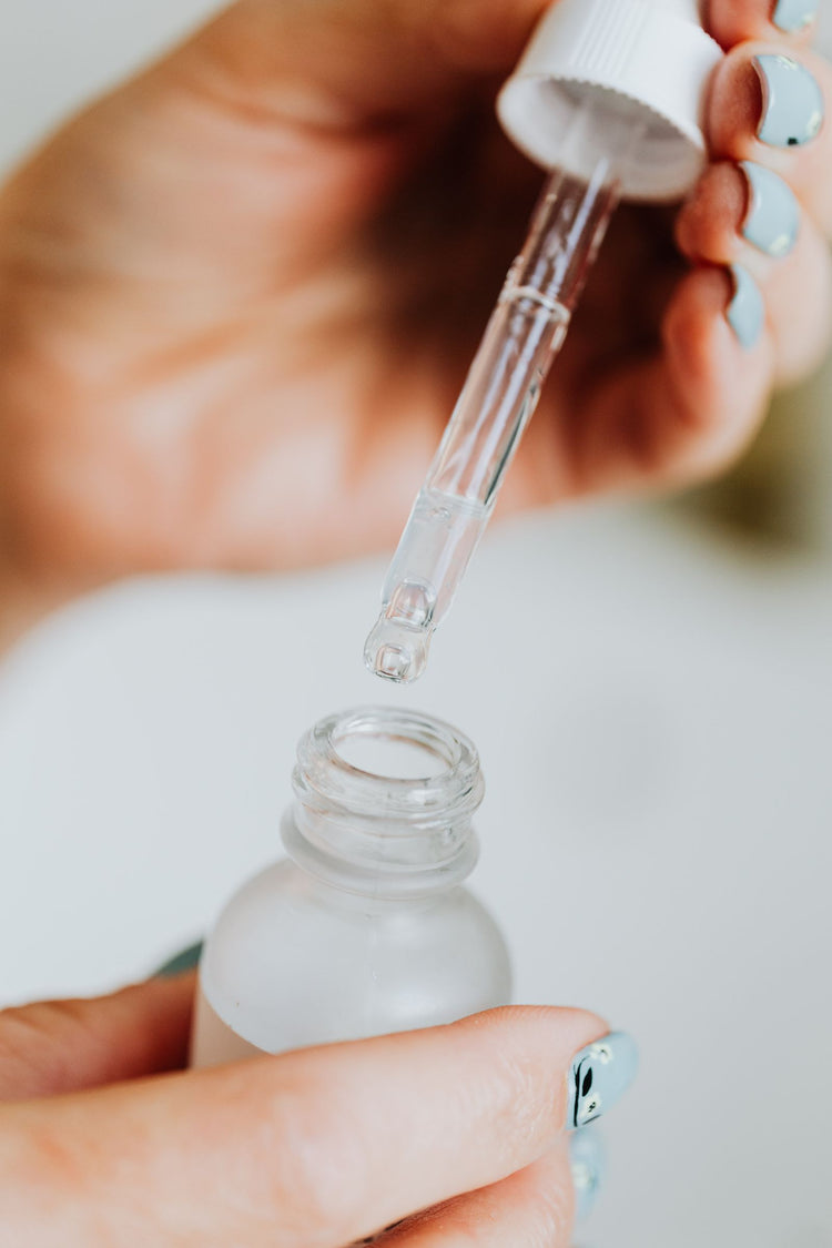 Mano aplicando suero facial con gotero desde un frasco de vidrio esmerilado