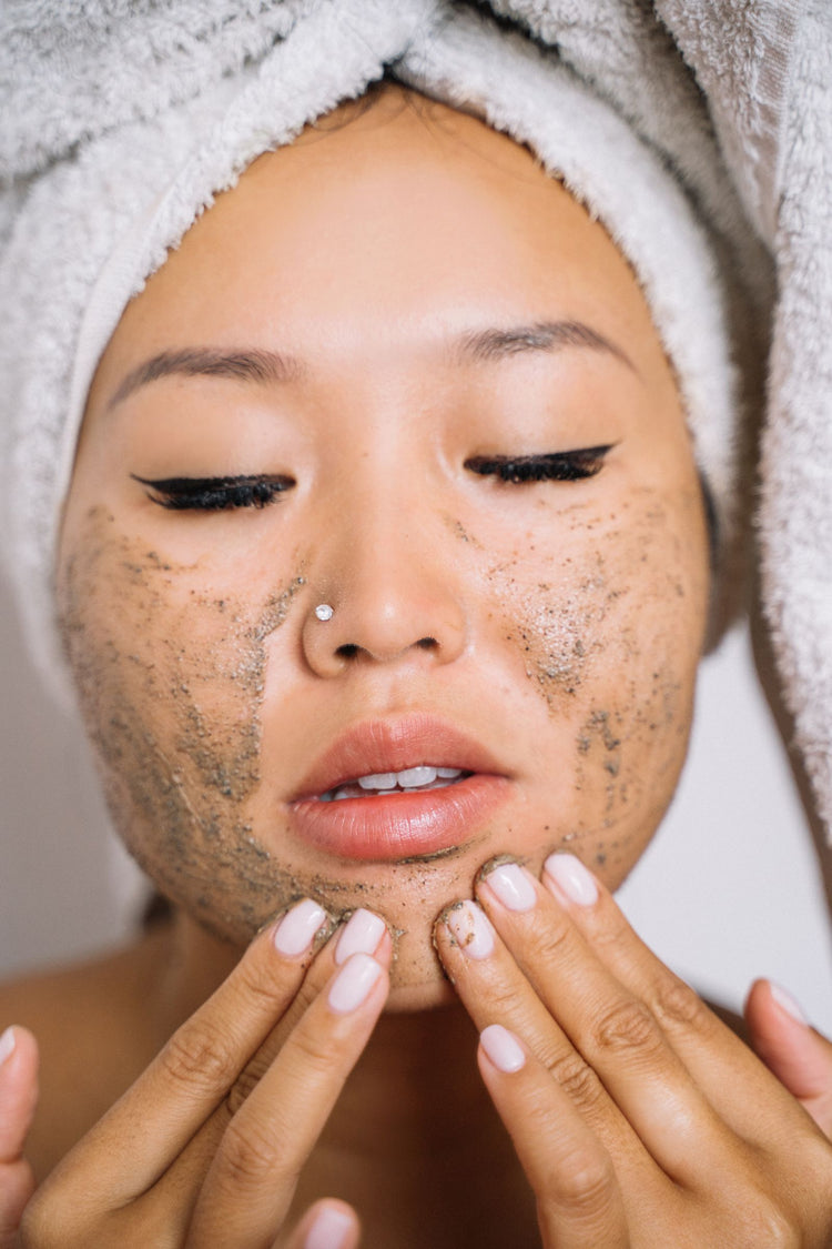 Mujer con toalla en la cabeza aplicando exfoliante facial